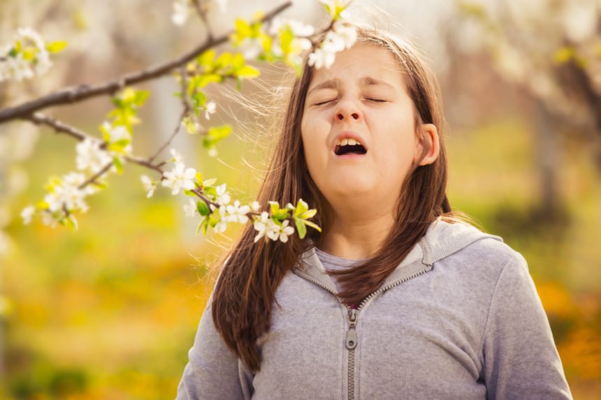 girl with brown hair about to sneeze under blooming tree branch