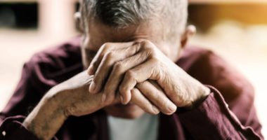 elderly man wringing hands in front of face.