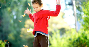 Action shot of boy tossing autumn leaves up into the air.