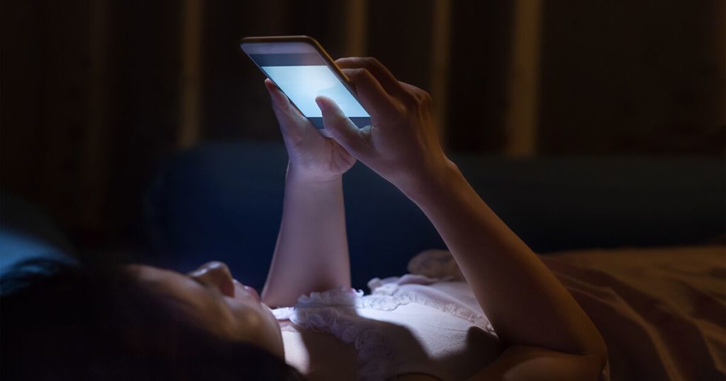 woman lying in bed looking at a smart phone