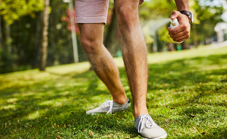 Close-up of man's legs being sprayed with insect repellent in the park outdoors