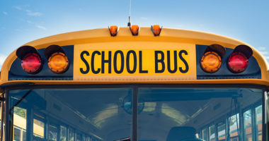 Front view of a yellow school bus against a blue sky.