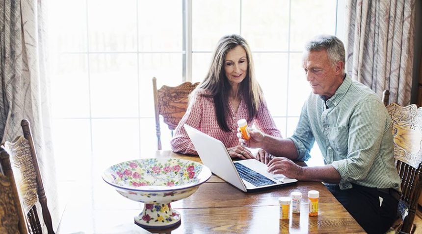 Older couple sitting at kitchen table, looking at laptop