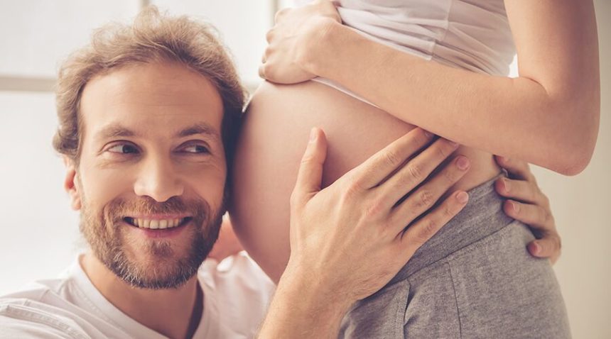 Man with ear on pregnant woman's belly