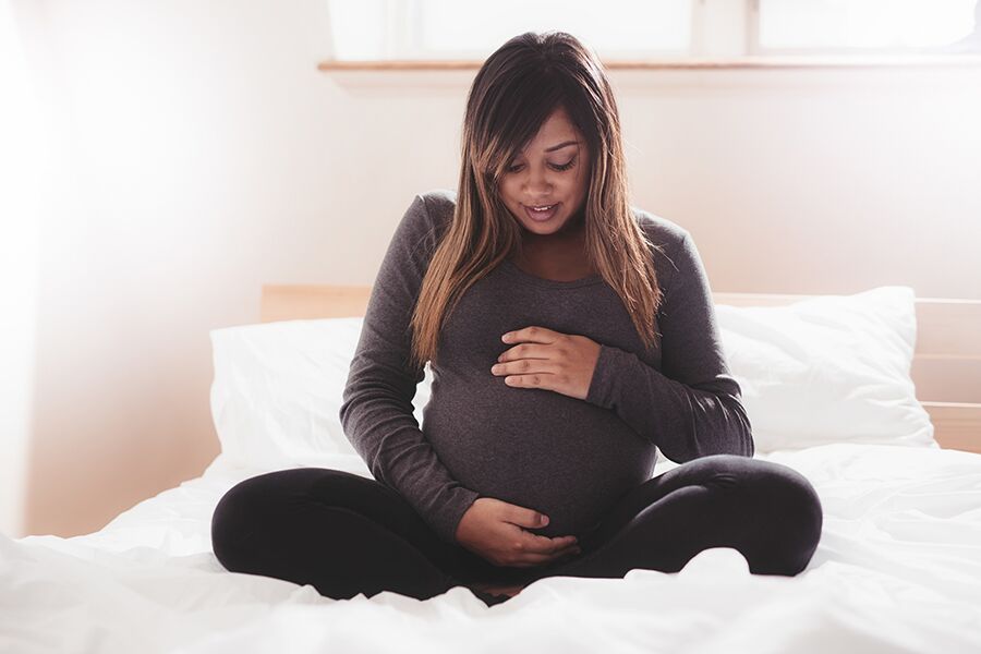 Pregnant woman sitting on a bed, looking at belly