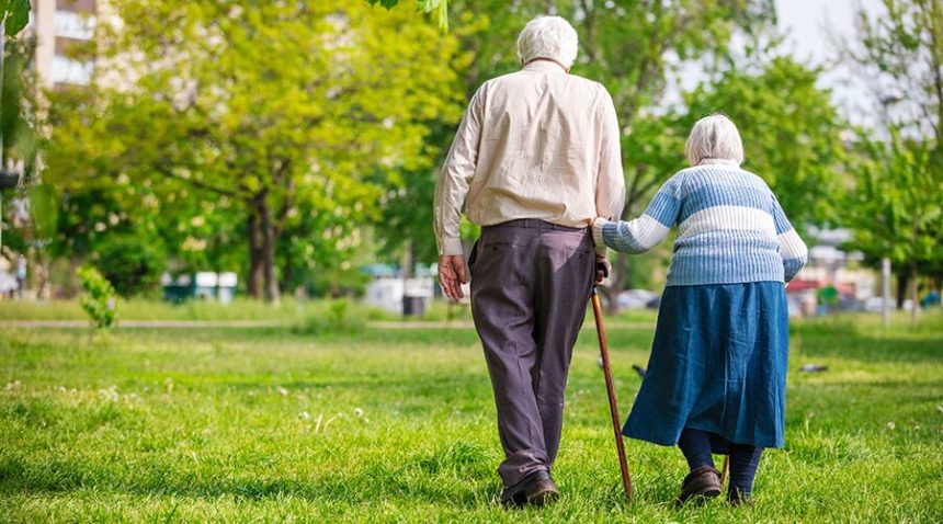photo of backs of old couple as they walk in the park