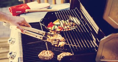 Person grilling meat and vegetables on a gas grill.