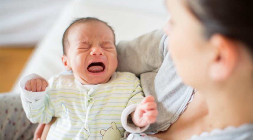 close-up photo of newborn crying while his mother holds him