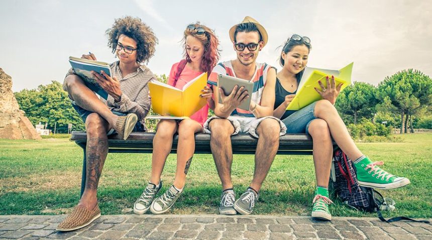Four college students sitting on a bench, reading books