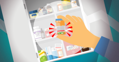 Hand holding a medicine bottle in front of a cabinet full of other medications