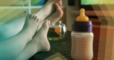 Photo of adult and child with feet propped up watching TV with beer and baby bottle on coffee table.