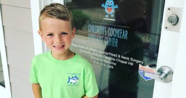 A photograph of Sam Hollamon outside of the entrance to the UNC Children's Cochlear Implant Center.