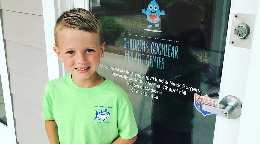 A photograph of Sam Hollamon outside of the entrance to the UNC Children's Cochlear Implant Center.