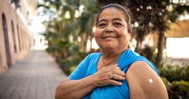 Woman in her mid-fifties holds up her sleeve proudly to show a bandage covering a flu shot injection site