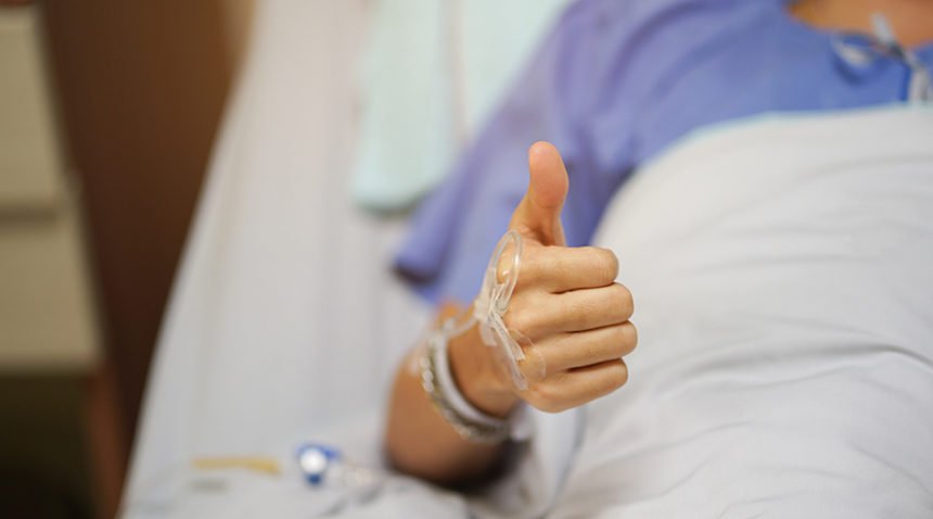 Patient giving a thumbs up in hospital bed.