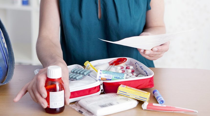 A photograph of a woman packing a first aid kit with medicine.