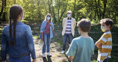 multi-generational family, all wearing face masks, stands in circle in forest clearing