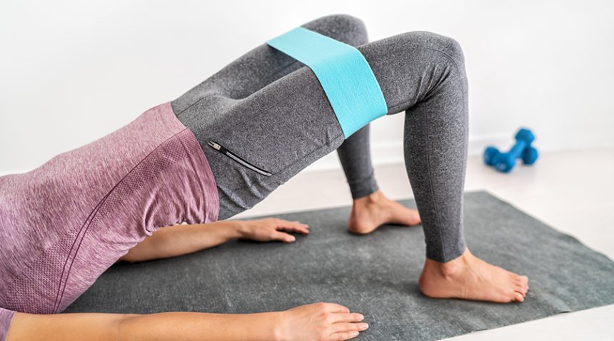Woman doing hip bridge on exercise mat, using elastic band