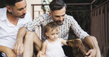 two fathers with their toddler daughter, playing with dachshund puppy
