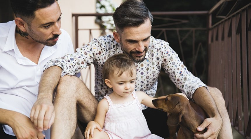 two fathers with their toddler daughter, playing with dachshund puppy