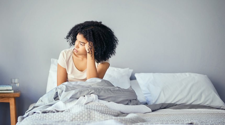 young woman sitting in bed, looking to the side, looking depressed