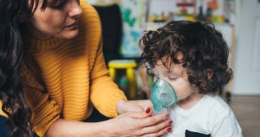 mother helps young child use a nebulizer machine