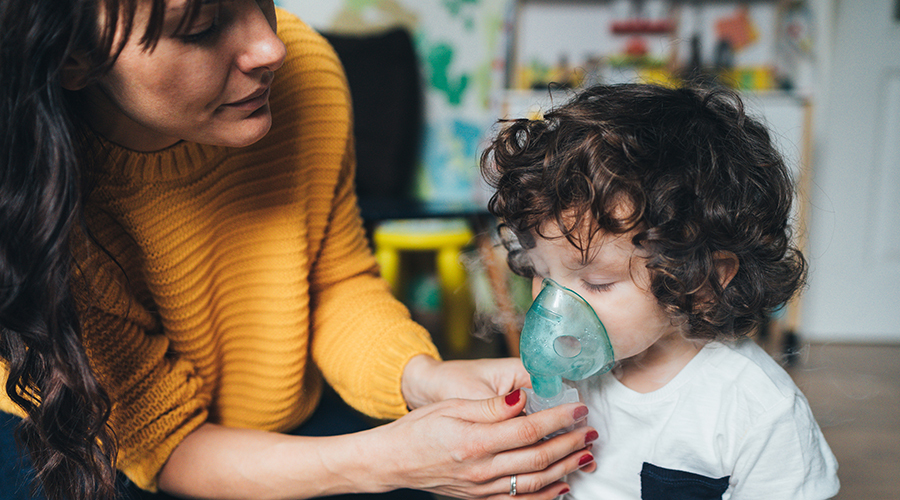 mother helps young child use a nebulizer machine