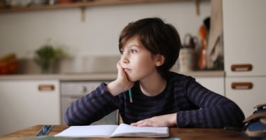 boy sits at kitchen table with pencil and paper, looks reflectively out the window