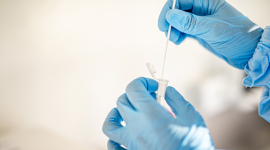 medical person, wearing gloves, places swab into a vial