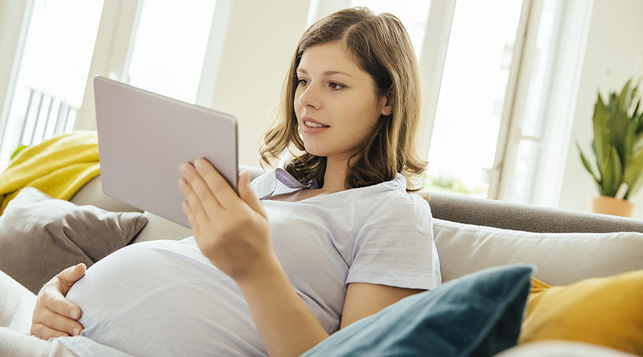 pregnant woman sitting on couch, talking to tablet