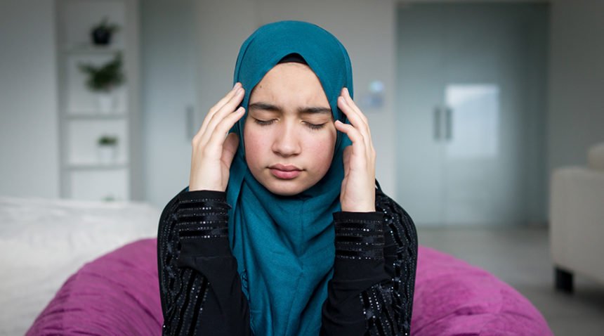 woman wearing hijab scarf rubs temples, looks stressed