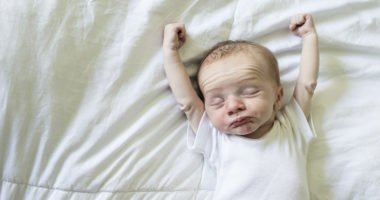 newborn baby stretches their arms over their head, eyes closed