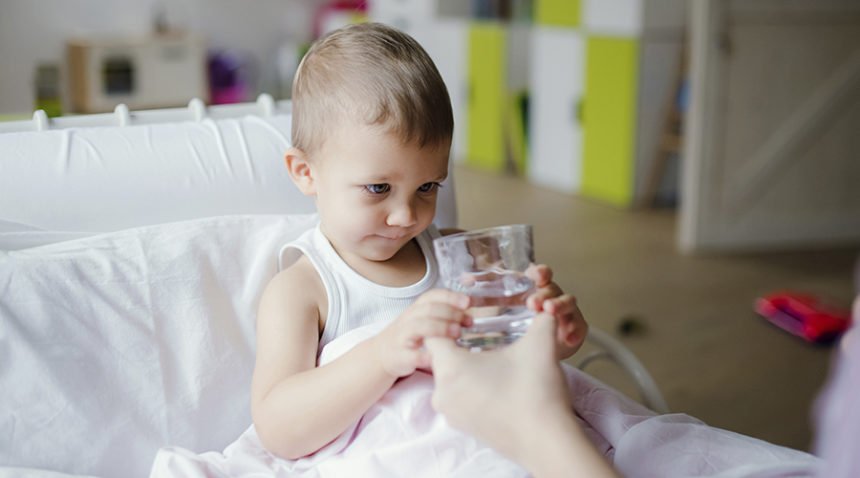 toddler girl takes glass of water from mother