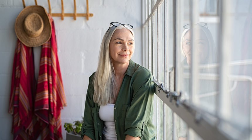 woman with long white hair looks out of window