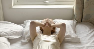 woman lying down on bed with her hands over her eyes in frustration