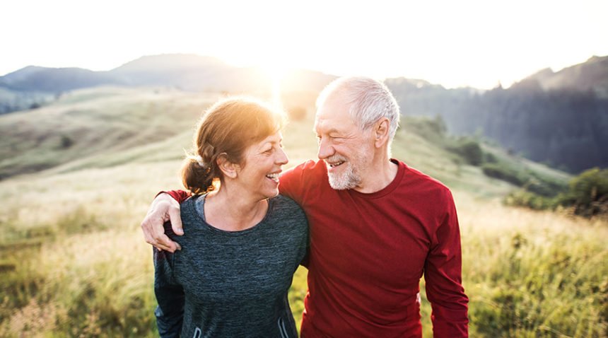 older couple smiles at each other on top of a mountain, sun beam peaking through between their heads