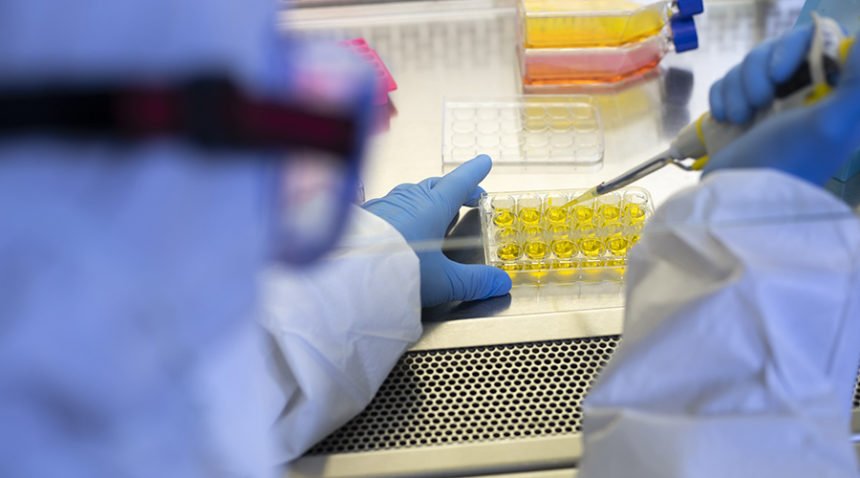 Over-the-shoulder shot of Researcher in full protective gear uses syringe in lab