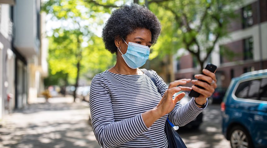 Older woman wearing mask looks at her phone while out on a city street