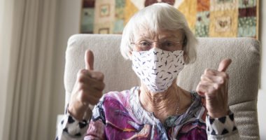 Older woman wearing face masks gives a 'thumb's up' to the camera
