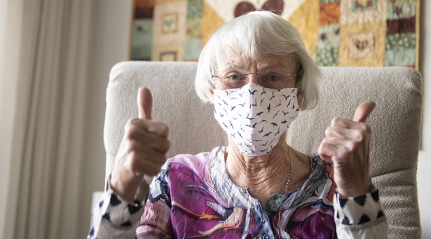 Older woman wearing face masks gives a 'thumb's up' to the camera