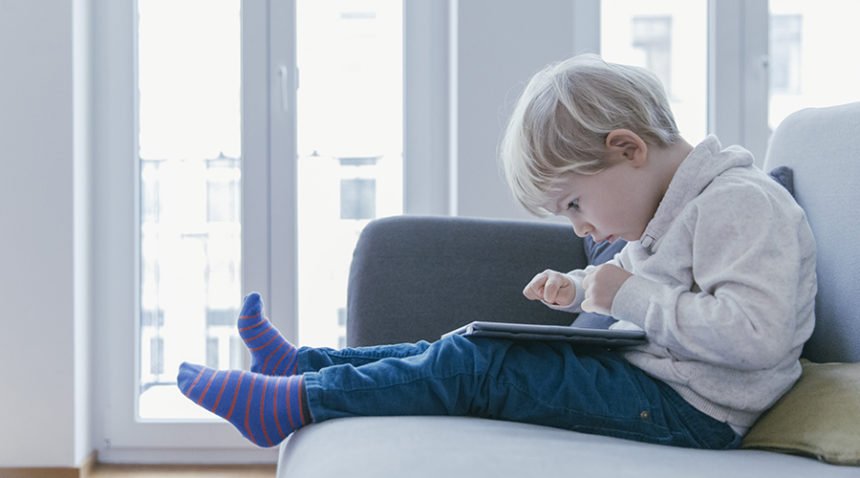 Little boy sits on couch, hunched over to watch tablet in his lap