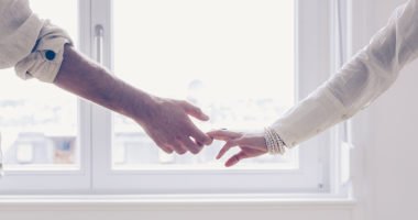 Closeup image of couple holding hands while standing by a window