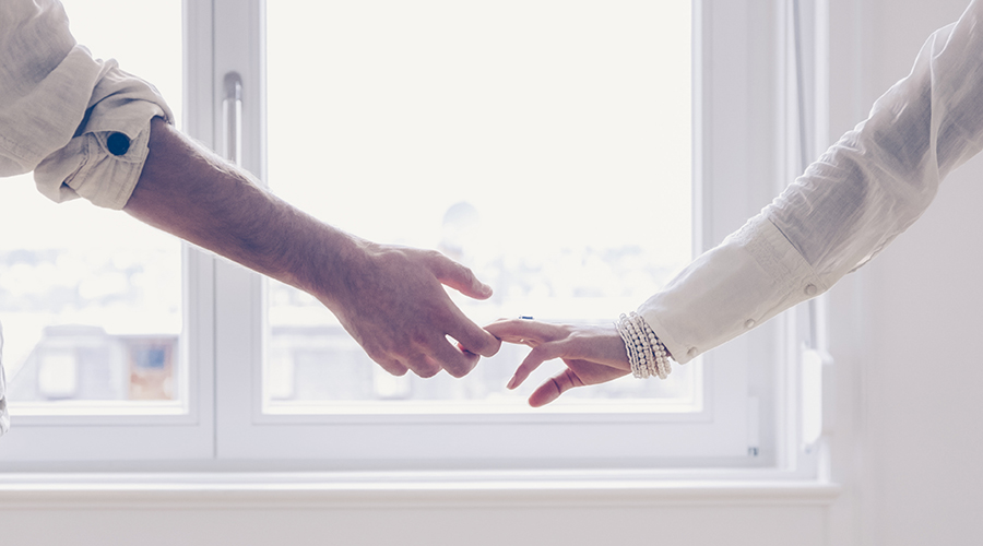 Closeup image of couple holding hands while standing by a window