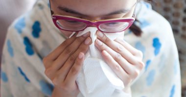 A young woman is having a flu and using a tissue paper to sneeze