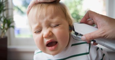 a toddler with a runny nose fusses as an adult takes their temperature in their ear