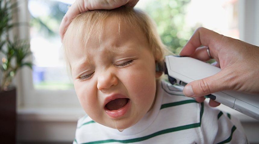 a toddler with a runny nose fusses as an adult takes their temperature in their ear