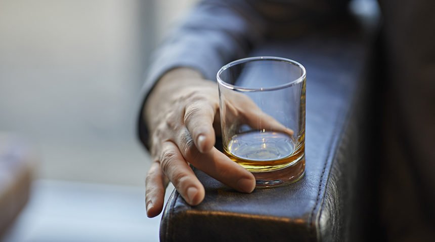 Close-up of man with whiskey glass on arm rest of a leather chair