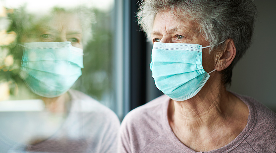 older woman wears a face mask while she looks out the window