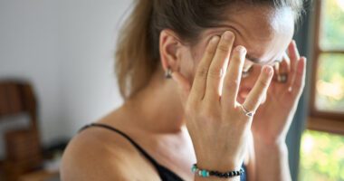 A woman holds her head while looking overwhelmed or not feeling well.