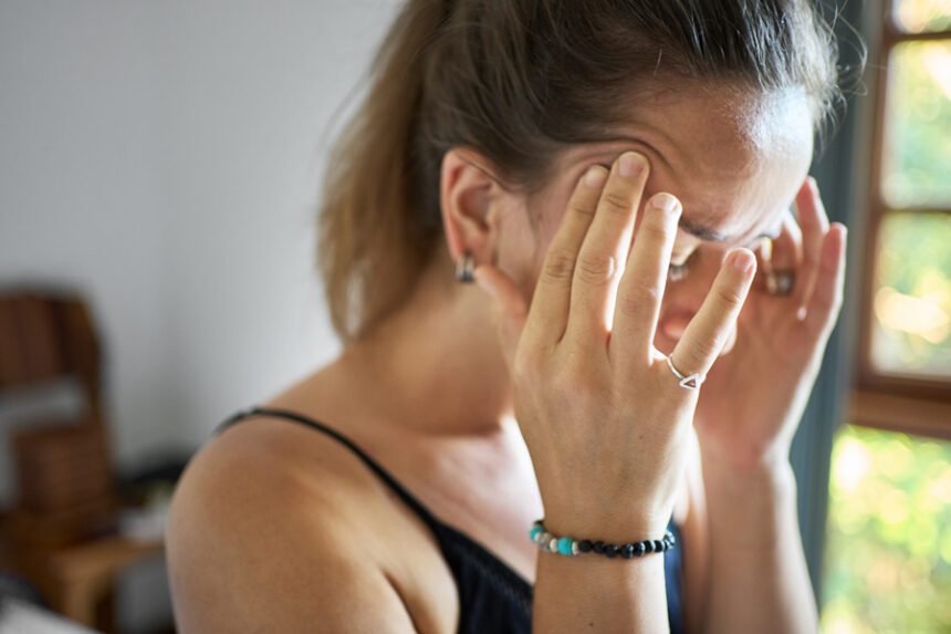 A woman holds her head while looking overwhelmed or not feeling well.